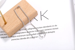 Long silver tassel chain earring with open hoop detail on a minimalist wood and paper backdrop