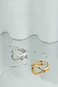 Detail of minimalist wave silver and gold rings on a reflective water drop surface