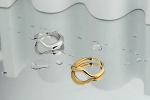 Detailed view of dual-tone wavy silver and gold open rings on a reflective water surface