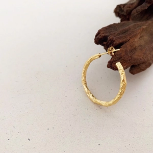Close-up of golden hoop earring with unique hammered foil texture on artistic wood stand