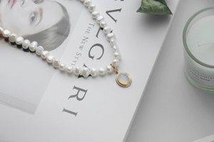 Detailed close-up of Baroque pearl necklace with gold moonstone pendant on white background