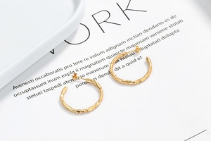Macro detail of gold C-shape earrings with irregular hammered texture on white card