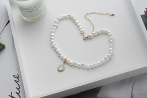 Flat lay of baroque pearl necklace with oval opal pendant and adjustable gold clasp