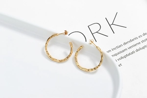 Detail of gold circular drop earrings with hammered texture on a white ceramic plate