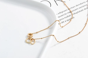 Detail of gold triple-interlocked rings necklace with zircon on white porcelain tray