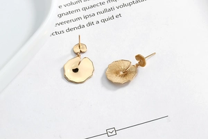 Close-up of golden leaf stud earrings featuring mirror polish and brushed texture detail