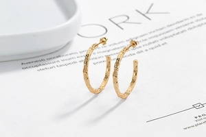Macro detail of gold C-shaped hoop earrings with handcrafted hammered texture and butterfly back