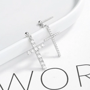 Macro view of silver cross pendant earring with zircon stones on white ceramic edge