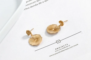 Macro shot of gold-plated lotus leaf drop earrings showing delicate pleated metal textures