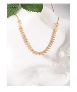 Close-up of golden leaf-shaped choker necklace on a white ceramic background with flowers
