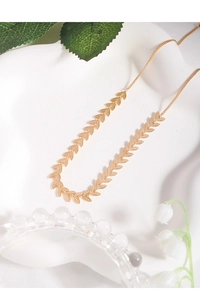 Detailed macro shot of a shiny gold leaf-shaped choker necklace on a white ceramic tray