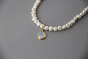 Detail of baroque pearl necklace with gold moonstone pendant on grey background