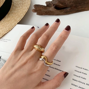 Close-up of minimalist wave pattern and wide gold rings worn by model in vintage setting