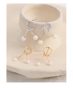 Detail of rope knot pearl earrings in gold and silver finish on a ceramic bowl
