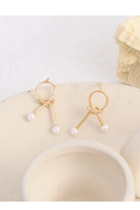 Detailed macro view of gold knotted hoop earrings with dangling double white pearls