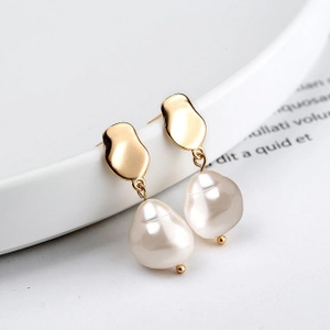 Macro shot of baroque pearl earrings with irregular gold geometric metal on white ceramic