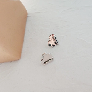 Macro shot of molten-style silver heart earrings on a minimalist textured white surface