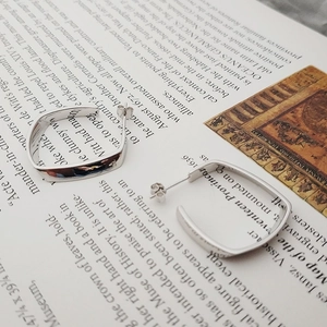 Detailansicht quadratischer Creolen aus poliertem Silber auf Vintage-Buchhintergrund