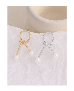 Macro detail of knot design pearl earrings in gold and silver finish on textured background