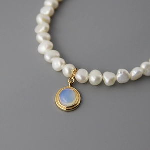 Baroque pearl necklace with a gold-plated round moonstone pendant on gray background