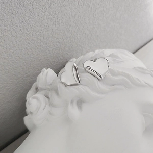 Artistic detail of heart-shaped silver earrings displayed on a white plaster sculpture