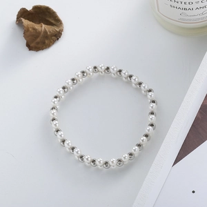 Detailed view of layered silver beads and white pearls woven in a spiral bracelet pattern