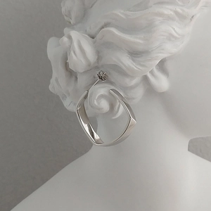 Detail eines gedrehten silbernen Ohrrings mit Politur auf einer minimalistischen Büste