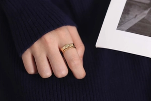 Detail of wavy golden ring with lava texture worn on index finger with blue knit background