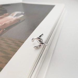 Macro detail of silver interlocking double-C ear cuff on white book page