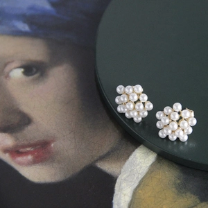 Close-up of cluster pearl earrings with gold base against artistic painting backdrop