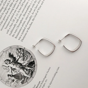 Makroansicht silberner geometrischer Creolen mit poliertem Finish auf einem Buchblatt