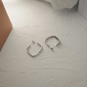 Nahaufnahme minimalistischer geometrischer Silberohrringe auf weißem strukturiertem Stein