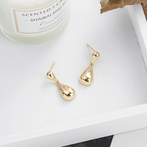 Macro view of gold teardrop earrings with pavé crystals on a white wooden tray