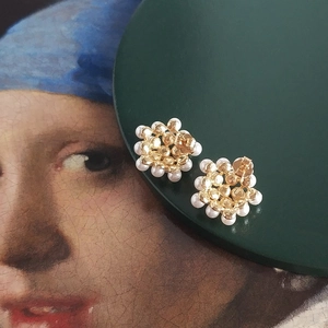 Close-up of golden cluster pearl stud earrings on an artistic classical painting background