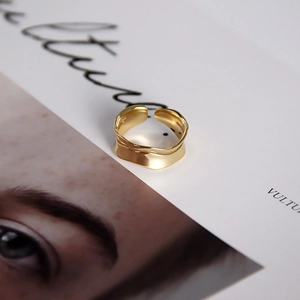 Detail of a wide gold-plated wavy ring showcasing flowing edges on a magazine backdrop