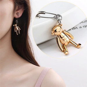 Detail of silver safety pin earring with a shiny gold bear pendant on model and close-up