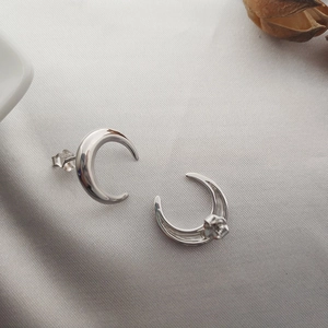 Macro detail of crescent moon S925 sterling silver stud earrings on soft silk fabric