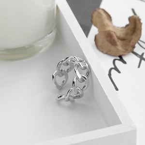 Detailed close-up of a silver chain ring with a hollow heart link on a white tray