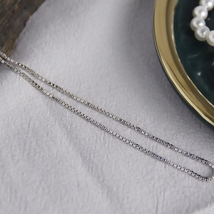 Gros plan d'un collier chaîne box argenté minimaliste sur tissu blanc texturé