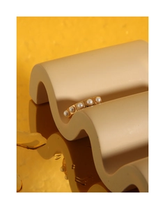 Detail of five white pearls set in linear gold square frames on a wave display