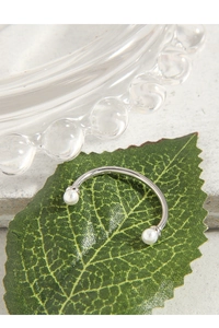 Detail view of a 925 silver C-shaped open ring with dual pearls on a green leaf