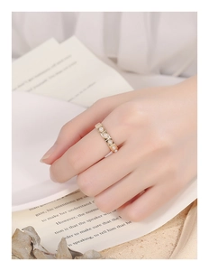 Detailed close-up of a gold thin ring with square frames and white pearls on a hand