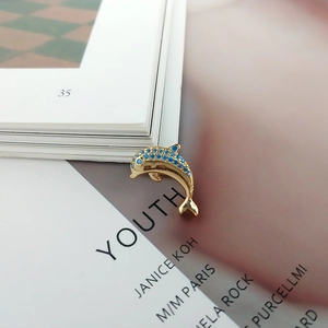 Detail of a golden dolphin earring inlaid with vibrant blue zircon stones on art paper