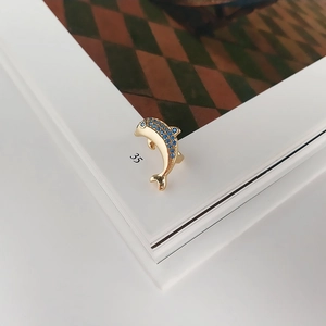 Detail of golden dolphin ear clip with blue zircon stones on a minimalist background