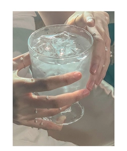 Close-up of minimalist 925 silver pearl rings on a hand against a glass with ice