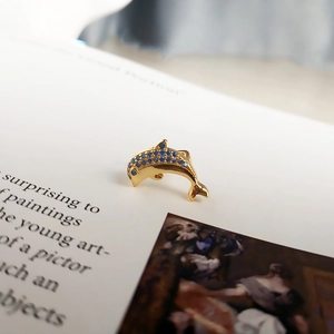 Macro shot of gold dolphin earring inlaid with blue crystals on vintage book background