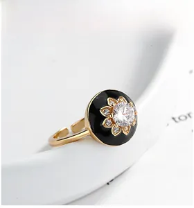 Macro view of gold flower ring with black enamel and diamonds on white plate