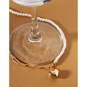 Close-up of gold heart pendant with asymmetrical pearl and paperclip chain necklace