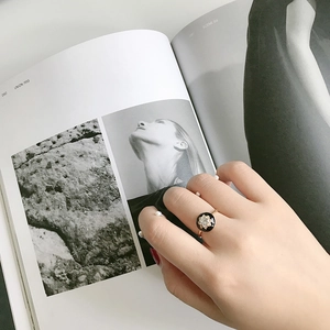 Elegant gold ring with black enamel and center stone shown on model finger over a magazine