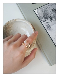 Détail d'une bague dorée ajustable ornée d'une perle blanche et d'une perle métallique